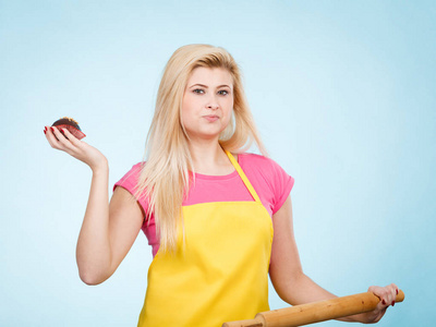烘烤美味甜点糖果被放在首页的概念。女人抱着美味的巧克力蛋糕和擀面杖穿着黄色围裙