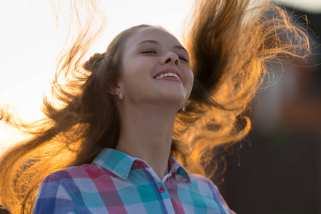 笑的年轻女她的长发背光的黄昏太阳在日落时的特写肖像照片