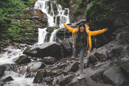 妇女站在黄色的雨衣, 看着瀑布。徒步旅行概念