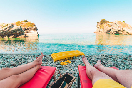 一对夫妇躺在太阳躺椅上, 美丽的海景与岩石。暑假