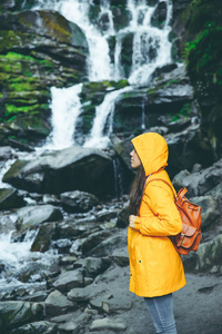 妇女站立在岩石在黄色雨衣与瀑布在背景。徒步旅行概念