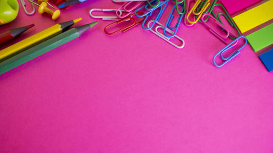 桌子上的铅笔和回形针。学校供应粉红色背景。从上面查看复制空间