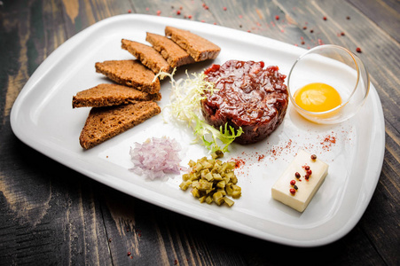 面包芯片牛肉配芝麻菜沙拉鞑靼,鸡蛋蛋黄和脆面包芯片在白板上照片