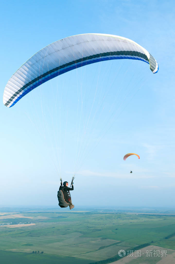 运动员在滑翔伞飞越上背景为蓝色的天空和其他运动员的字段照片-正版