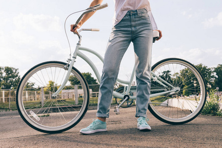 裁剪图像的穿牛仔裤与一辆自行车在公园里的女人照片