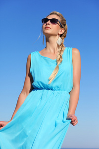 在一件蓝色连衣裙和太阳镜上天空背景中的女孩