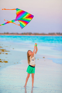 在日落和戏剧在大洋彼岸热带海滩上放风筝的小女孩。儿童沙滩玩具