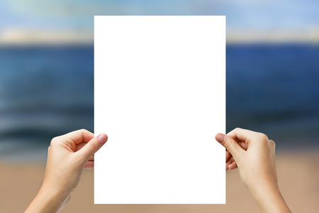 隔空双手拿着白纸,空白地隔在模糊的海背上照片