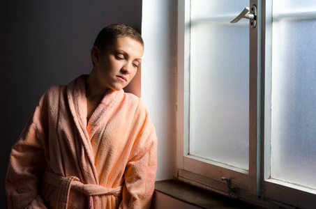 年轻女子癌症病人站在医院的窗户