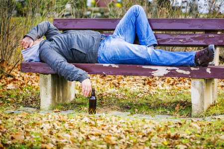 啤酒瓶在公园的长椅上睡觉的人