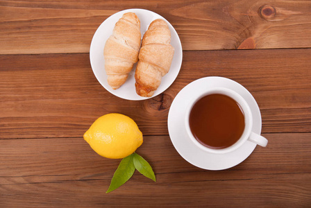 杯茶柠檬和羊角面包上木制的背景