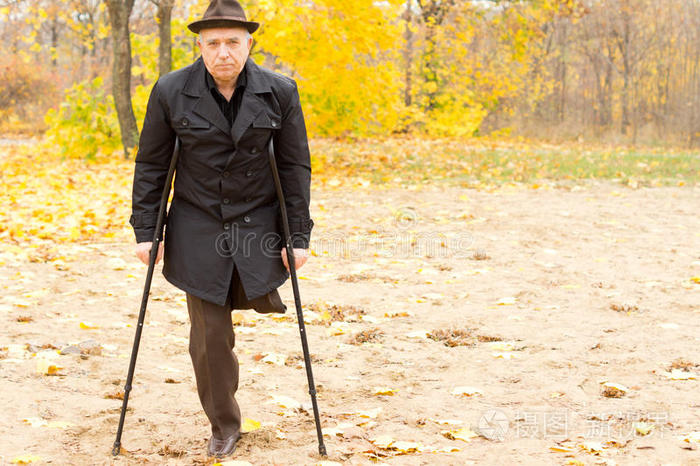 一条腿的男人拄着拐杖在公园里散步