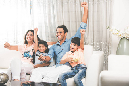 印度年轻家庭的 4 坐在沙发上同时观看电视一起，选择性焦点