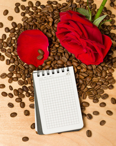 红玫瑰和笔记本上咖啡种子和木制背景