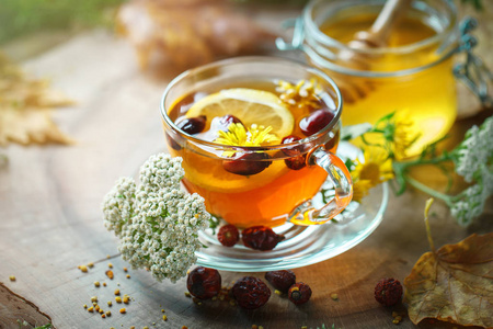 美味的新鲜蜂蜜和一杯健康茶与柠檬和玫瑰的臀部，木制的桌子上。选择性的焦点