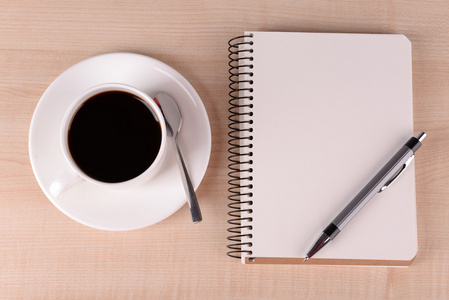 杯咖啡碟与笔记本和笔在木桌背景上