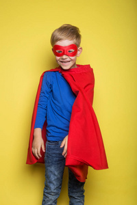 男孩在红的超级英雄和掩码。超人。在黄色背景的工作室画像
