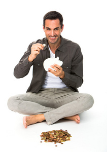 男人坐在地板上，微笑着摄像机，拿着一枚硬币放在储钱