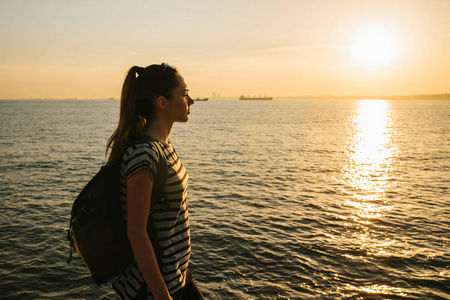 年轻游客的女孩背着日落时站在海边，眺望远方。休息 放松 旅行 度假