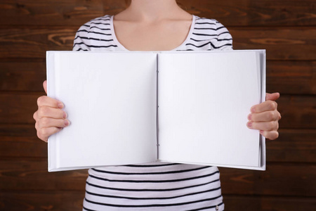 女人抱着打开书与木制背景上的空白页
