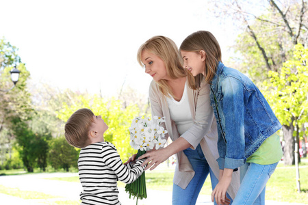 可爱的小男孩在春天公园里给他的祖母送花束在晴朗的天