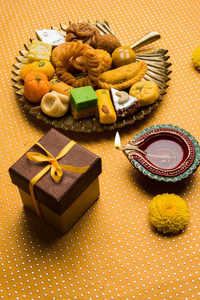 印度甜或 mithai 和油的灯或 diya 礼品盒和鲜花装饰或色彩缤纷的背景下，选择性焦点股票照片