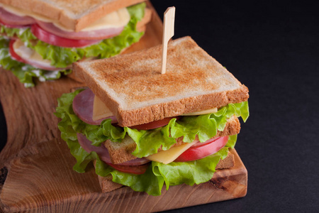 特写大三明治火腿 奶酪 西红柿和沙拉在烤面包上一个黑色的背景上