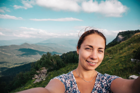 年轻女子的徒步旅行者微笑并考虑自拍照或智能手机的照片在山峰与山风景背景