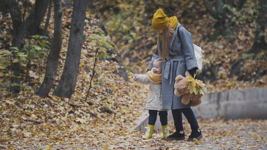 女人带着小女儿在黄色的树叶间的秋园