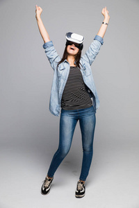 使用虚拟现实的护目镜的吸引力和幸福女人庆祝胜利的手势，在灰色的背景上。Vr 耳机