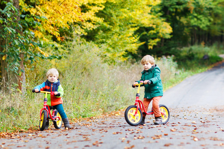 两个可爱的男孩驾驶自行车在秋天的树林