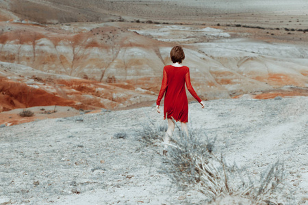 女人站在了美丽的红色的山谷中。她穿着一件漂亮的红色衣服。浪漫