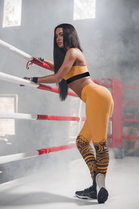 年轻的健身美丽的黑发女孩环靠在拳击台的绳子