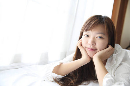 亚洲的年轻女子用枕头在白色的房间里醒来