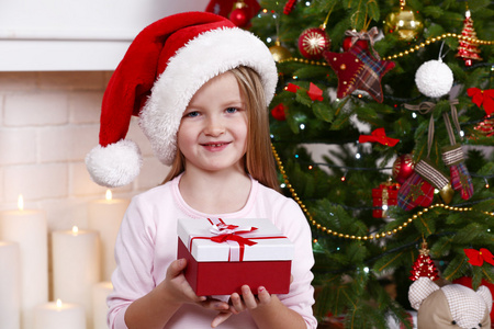戴圣诞帽的小女孩拿着圣诞树旁的礼物盒
