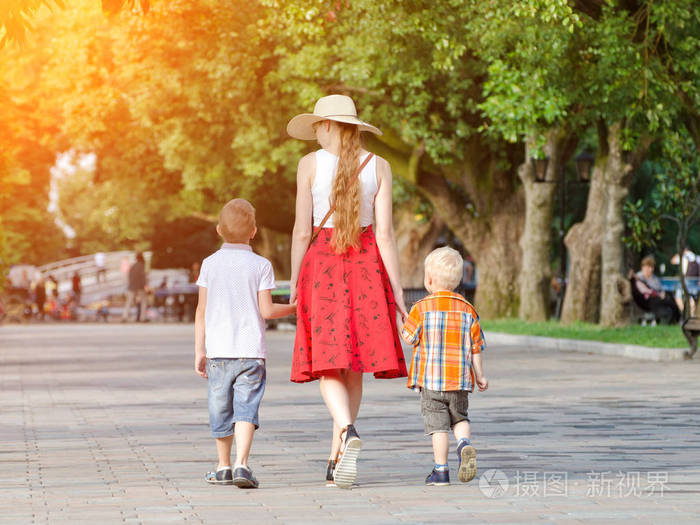 妈妈和两个儿子走在公园里阳光灿烂的日子查看从背面