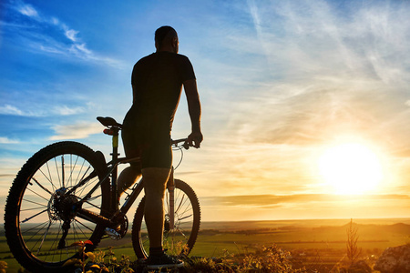 骑自行车的人站在一起在小山的山地自行车在日落时的剪影