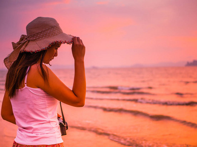 女人穿着近夕阳下的沙滩裙带帽子的海洋 旅游和度假的概念