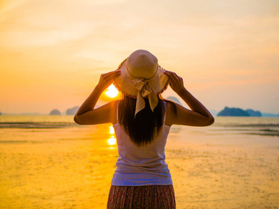 女人戴着顶帽子下附近日出的张开双臂的海洋 旅游和度假的概念