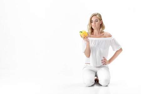 在白色的衬衫严重金发美女看黄色柿子椒。健康的饮食和饮食