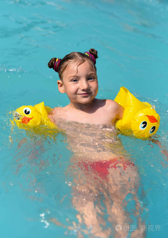 一个阳光明媚的享受玩和在游泳池里打开一个微笑的小女孩照片