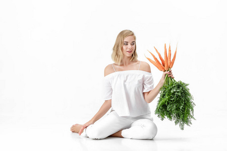 漂亮的金发女郎，拿着绿色的新鲜胡萝卜叶在白色背景上。健康与饮食