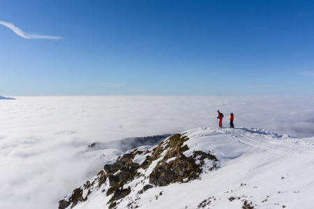 云层上方山顶上的两个滑雪者