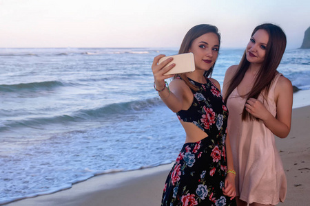 两个女孩制作自拍照磐石前的海滩上摆姿势
