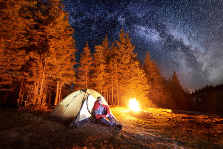 男人帐篷男人坐在靠近篝火和帐篷照片