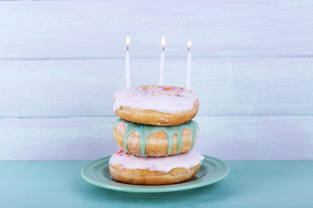 美味甜甜圈与结冰和生日蜡烛上木制背景表格