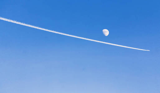 在湛蓝的天空白色的轨迹跟踪叶一架喷气式飞机。月亮