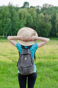 女孩的帽子和背包的绿色森林背景上握着头部后面的手