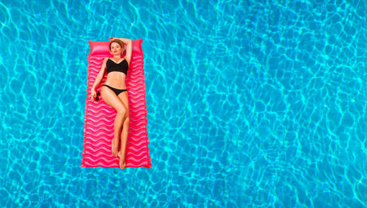 在游泳池里的充气床垫上比基尼的女人