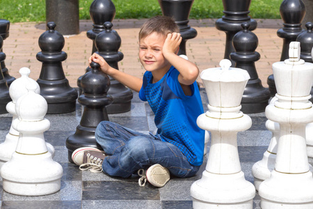 巨型象棋棋子的国际象棋游戏。男孩在黑色和白色的板上玩战略的户外游戏